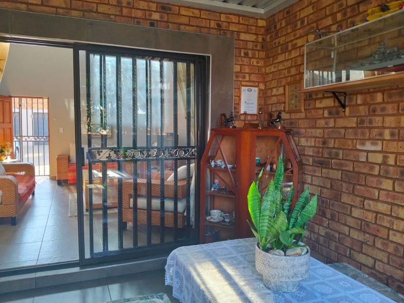 A covered patio area featuring exposed brick walls, tiled flooring, and a sliding glass door with a security gate leading into the home.