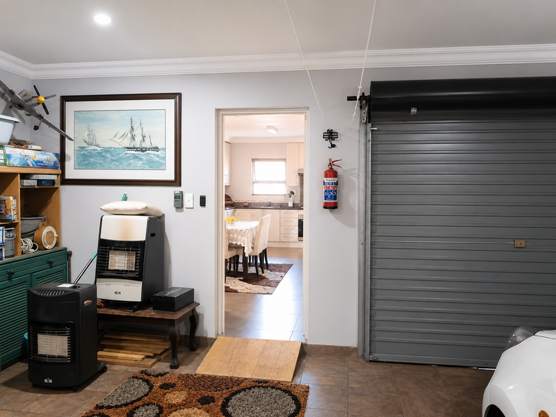 A well-maintained garage featuring a roller door, tiled flooring, and direct internal access to the kitchen area.