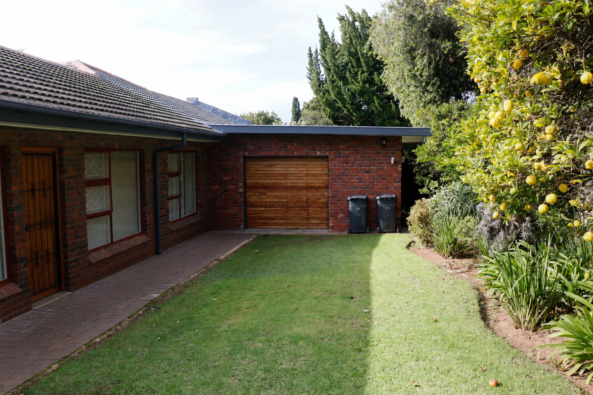 A view of the rear exterior featuring a brick facade, a paved walkway, a well-maintained lawn, and a wooden garage door.