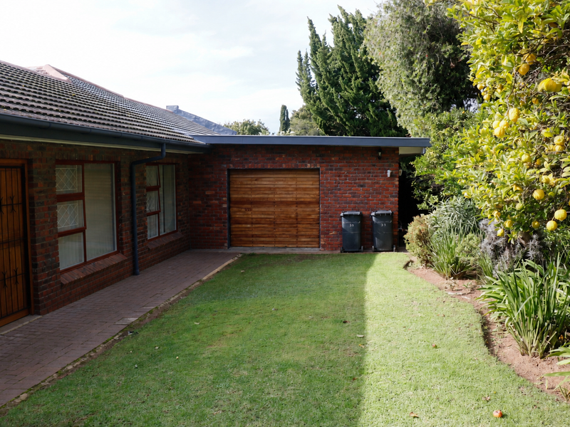 A view of the rear exterior featuring a brick facade, a paved walkway, a well-maintained lawn, and a wooden garage door.