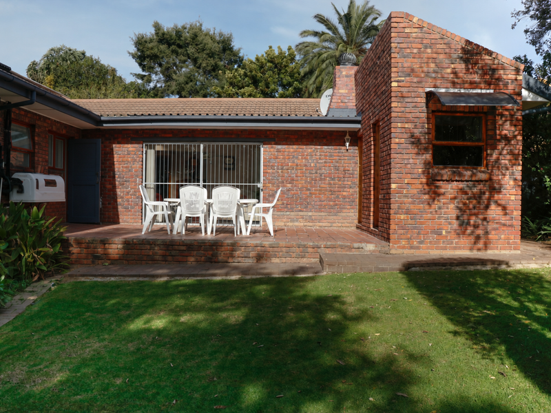 Rear view of the house featuring a brick facade, a paved patio area, and a well-maintained garden.