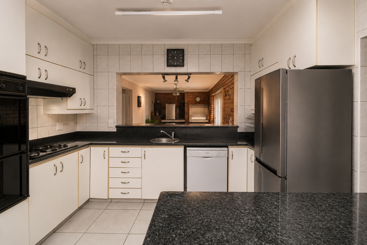 A functional kitchen featuring granite countertops, built-in oven, gas hob, and ample cabinetry, with a convenient serving hatch opening to the adjacent living area.