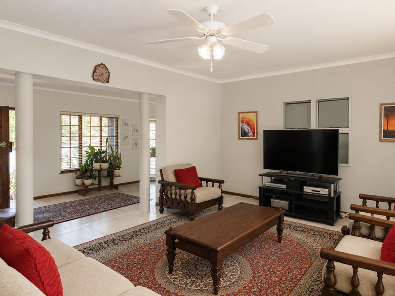 Spacious living room featuring tiled flooring, a ceiling fan, and architectural columns, providing an open and bright atmosphere with natural light.