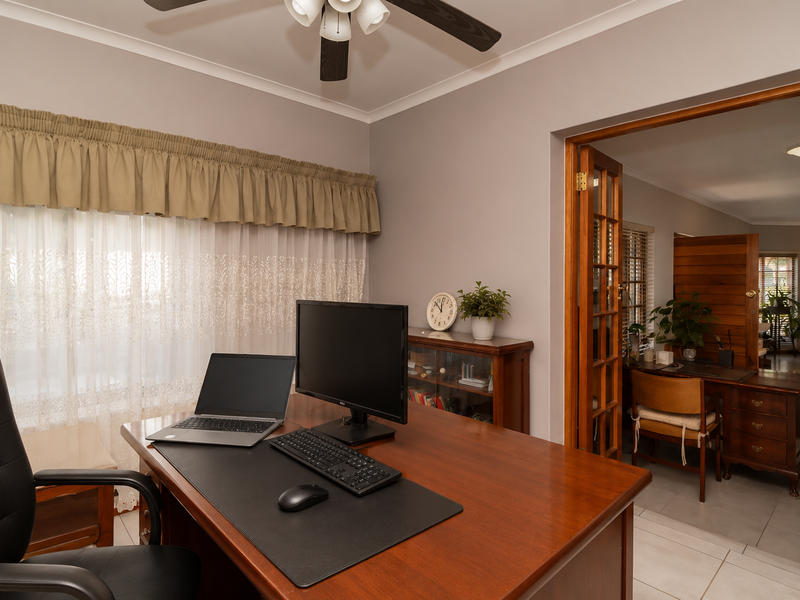 A functional home office featuring tiled flooring, a ceiling fan, and classic wooden french doors leading to an adjacent living space.