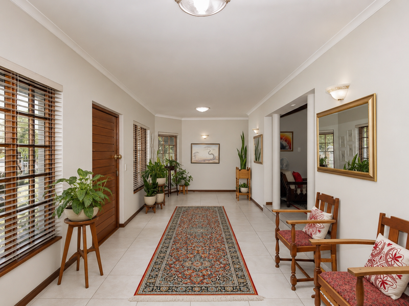 A spacious, well-lit hallway featuring neutral tiled flooring, wooden window frames with venetian blinds, and elegant wall sconce lighting.