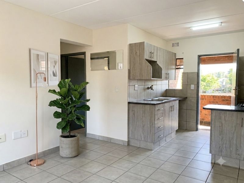Open-plan kitchen area featuring modern laminate cabinetry, stone-look countertops, and neutral ceramic floor tiles with direct access to an outdoor balcony.