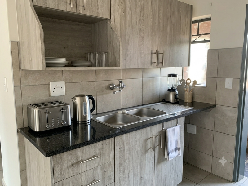 A functional kitchen area featuring wood-look laminate cabinetry, a granite countertop, and a stainless steel double sink with wall-mounted plumbing.