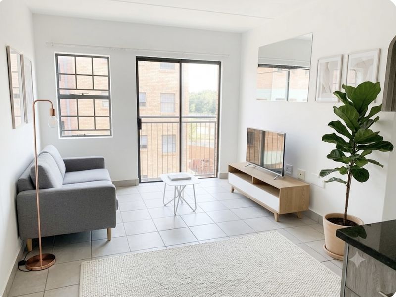 A bright and modern living room featuring tiled flooring, large windows, and a sliding glass door leading to a balcony.