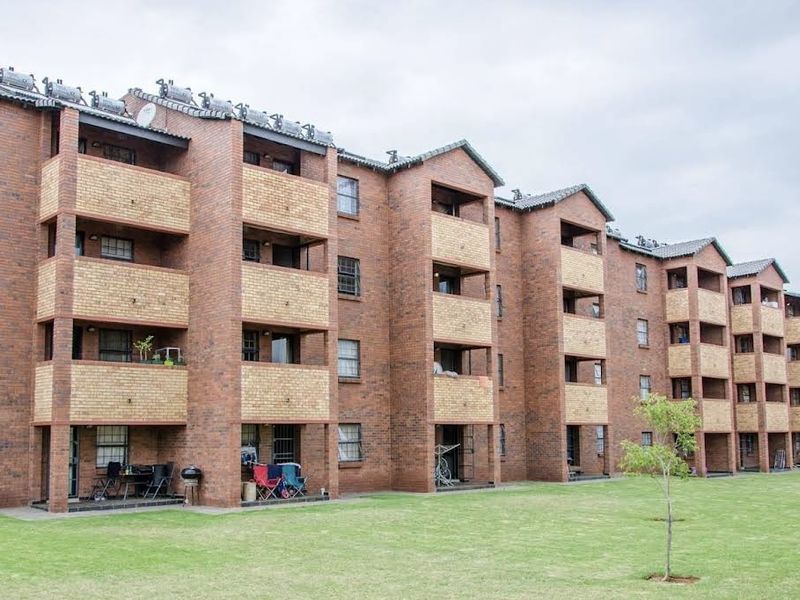 A multi-story apartment complex featuring face brick construction, private balconies for each unit, and solar water heating systems overlooking a communal garden area.