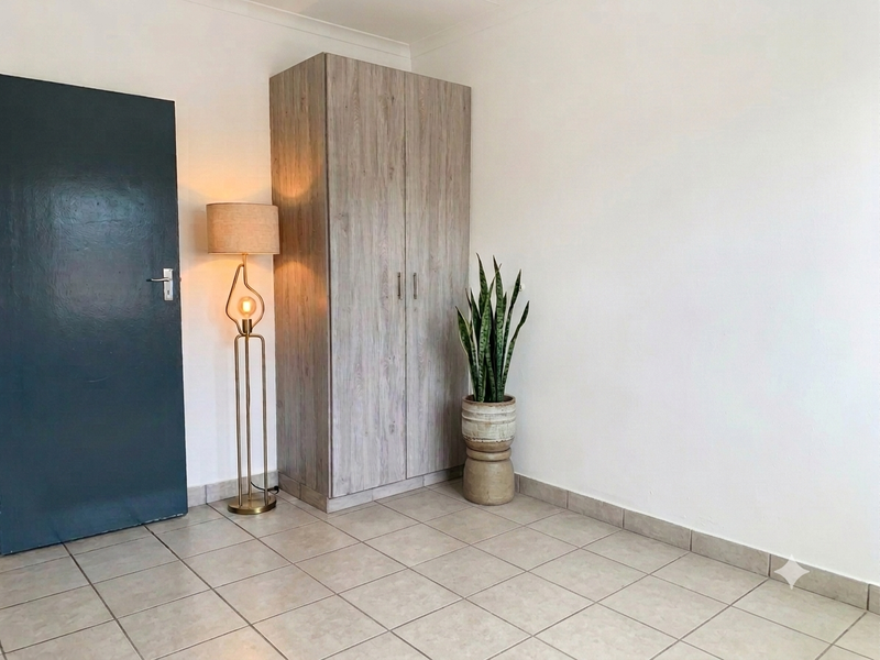 A clean, neutral bedroom featuring tiled flooring, coving, and a built-in wood-finish wardrobe.