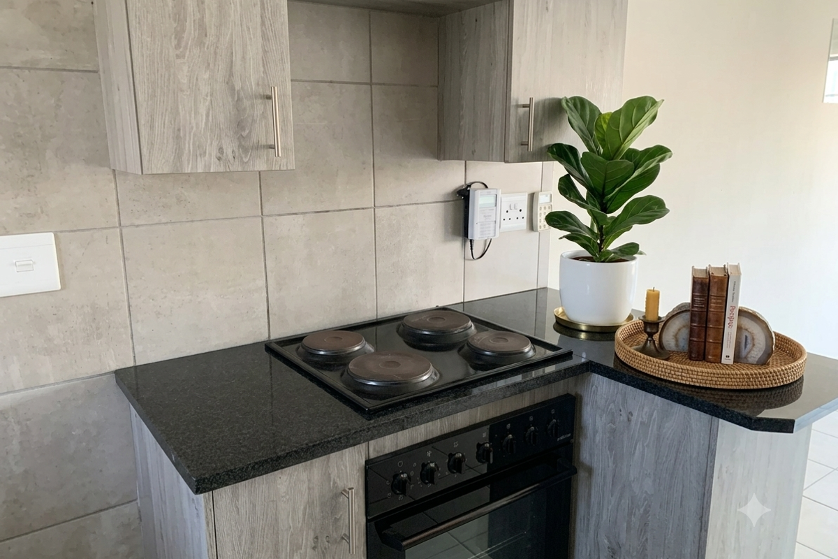 Modern kitchen area featuring grey wood-grain cabinetry, black granite countertops, and a built-in electric hob and oven with a tiled backsplash.