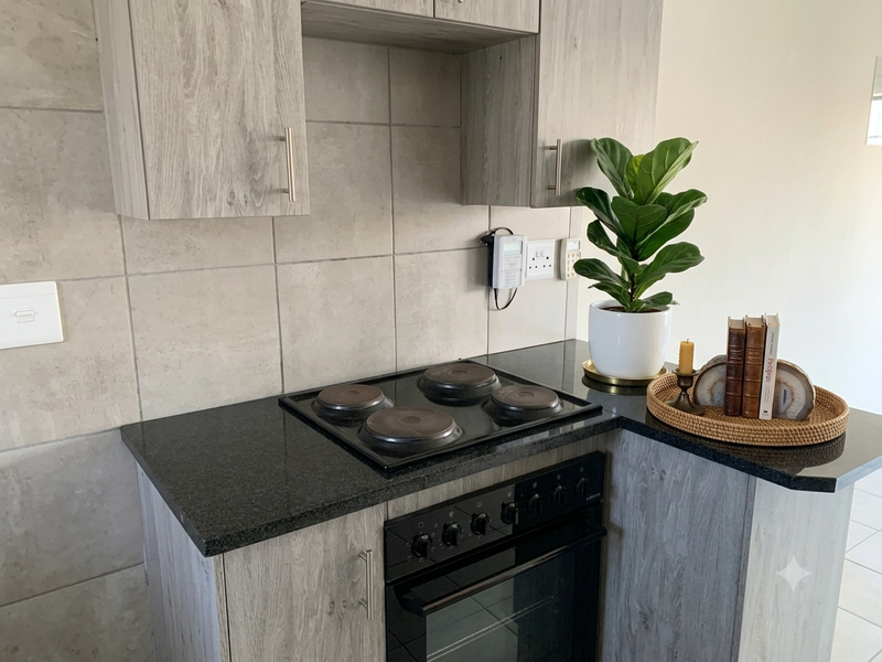 Modern kitchen area featuring grey wood-grain cabinetry, black granite countertops, and a built-in electric hob and oven with a tiled backsplash.