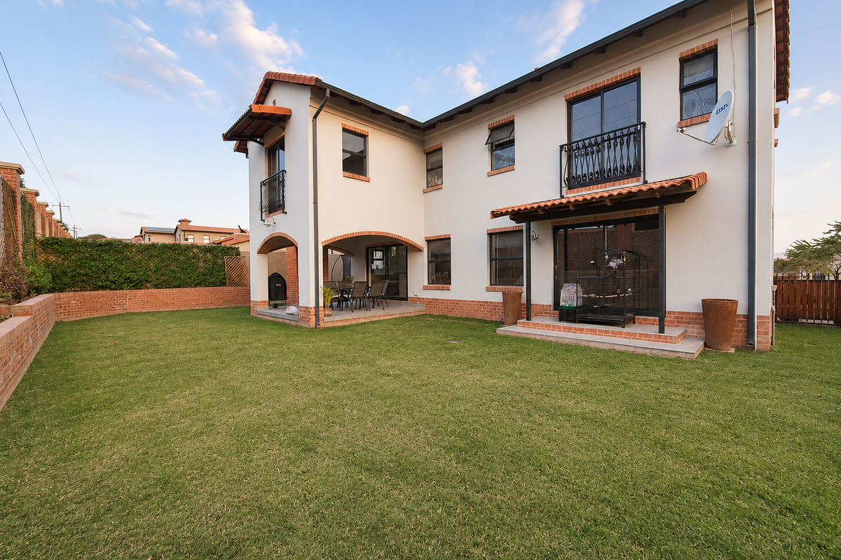 Rear view of a two-story house featuring a well-maintained lawn, covered patio area, and classic architectural details including tiled roofing and brick accents.