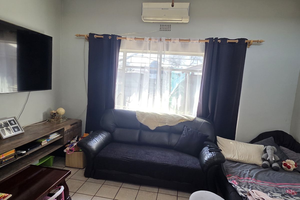 A functional living room featuring tiled flooring and a wall-mounted split-system air conditioner.