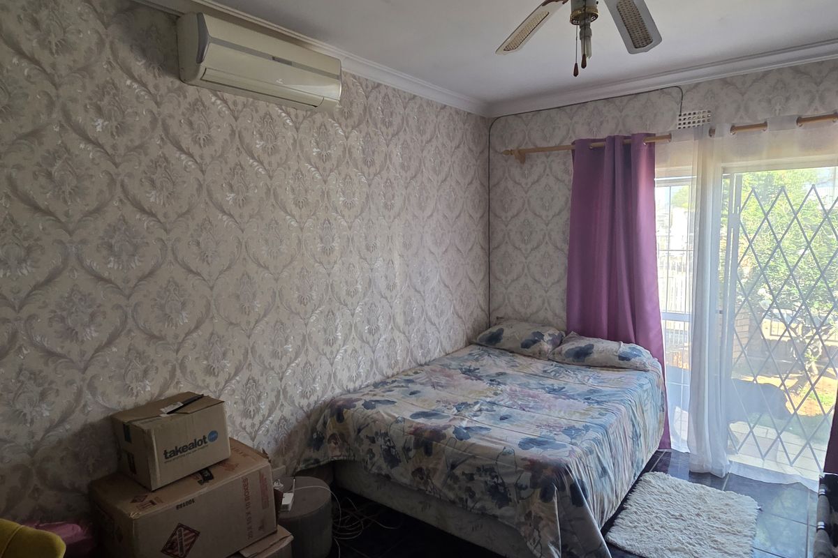A bedroom featuring tiled flooring, a ceiling fan, a wall-mounted air conditioner, and a sliding glass door with security gate access to the exterior.