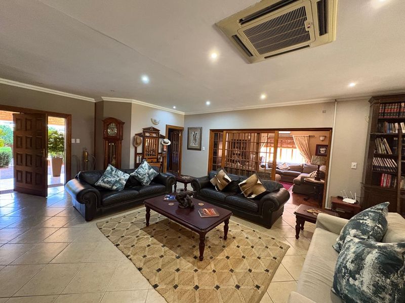 Spacious living room featuring tiled flooring, recessed lighting, ducted air conditioning, and a built-in wooden bookshelf, with access to an adjacent room via sliding doors.