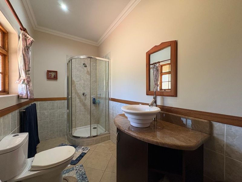A functional bathroom featuring a corner shower, vessel sink with granite vanity top, and tiled wainscoting with crown molding details.