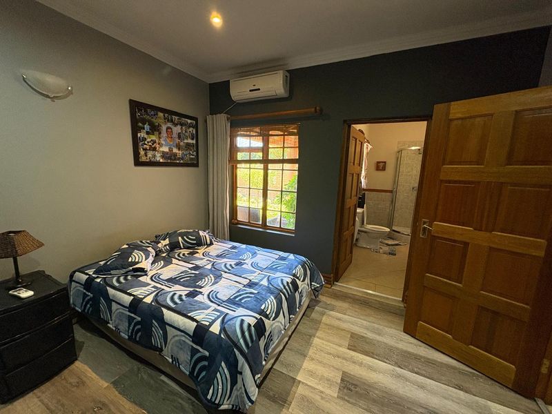 A well-maintained bedroom featuring laminate flooring, an integrated air conditioning unit, and direct access to an en-suite bathroom.