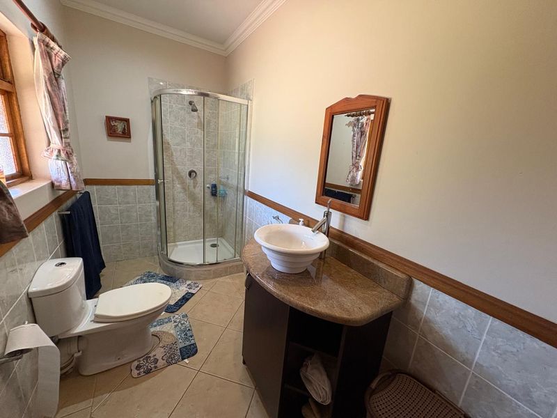 A functional bathroom featuring a corner shower enclosure, a vessel sink vanity, and neutral wall and floor tiling with decorative wood trim.
