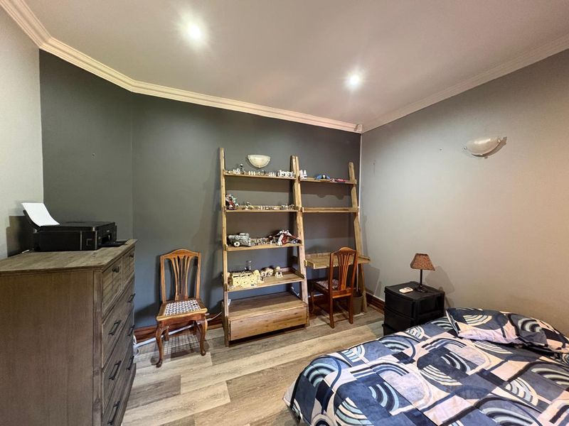 A bedroom featuring dark accent walls, crown molding, recessed lighting, and durable laminate flooring.