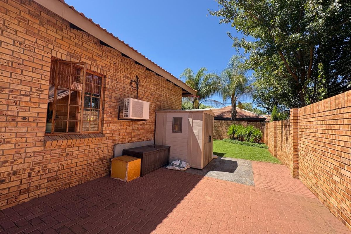 A private rear courtyard featuring a paved patio area, face brick exterior walls, and a small garden space enclosed by a perimeter wall.