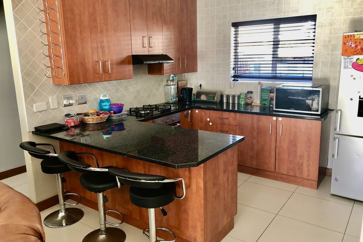A functional kitchen featuring granite countertops, wooden cabinetry, a gas hob with extractor fan, and tiled finishes throughout.