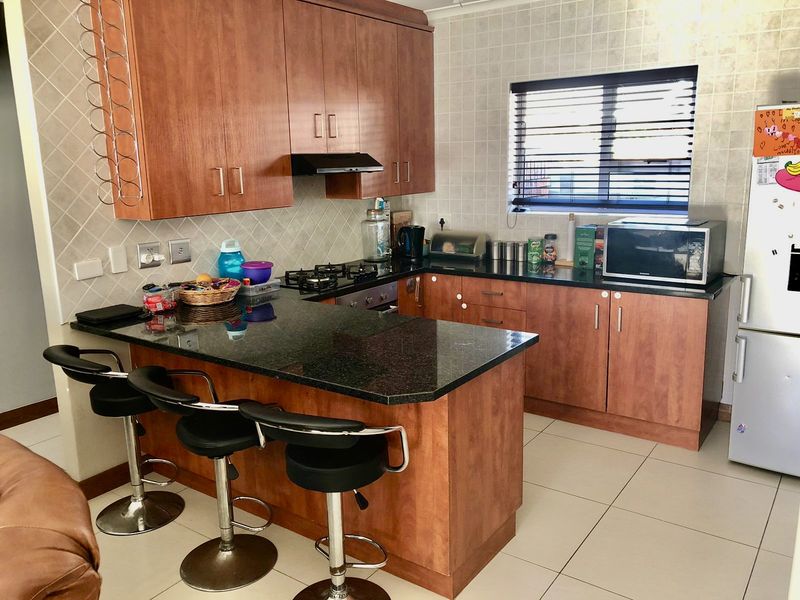 A functional kitchen featuring granite countertops, wooden cabinetry, a gas hob with extractor fan, and tiled finishes throughout.