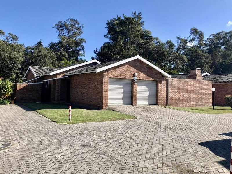 Front view of a brick townhouse featuring a double garage, paved driveway, and surrounding garden area.