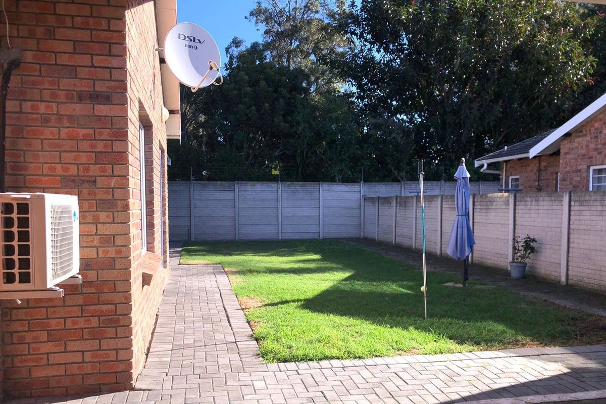 A private rear garden featuring a paved walkway, a small lawn area, and secure precast concrete boundary walls.