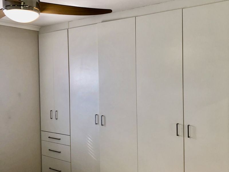A bedroom featuring extensive white built-in cabinetry with integrated drawers and a modern ceiling fan.