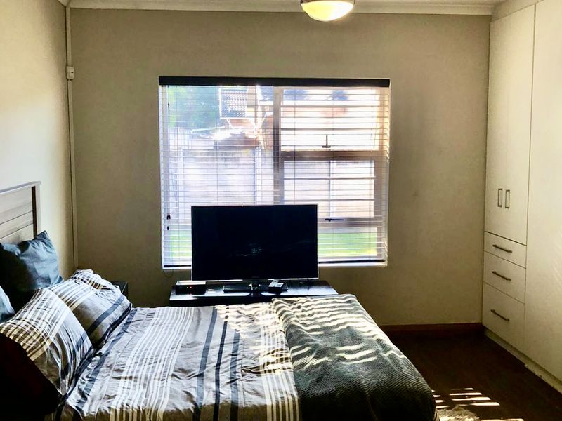 A well-lit bedroom featuring built-in cupboards, a ceiling fan, and venetian blinds, providing a functional and comfortable living space.