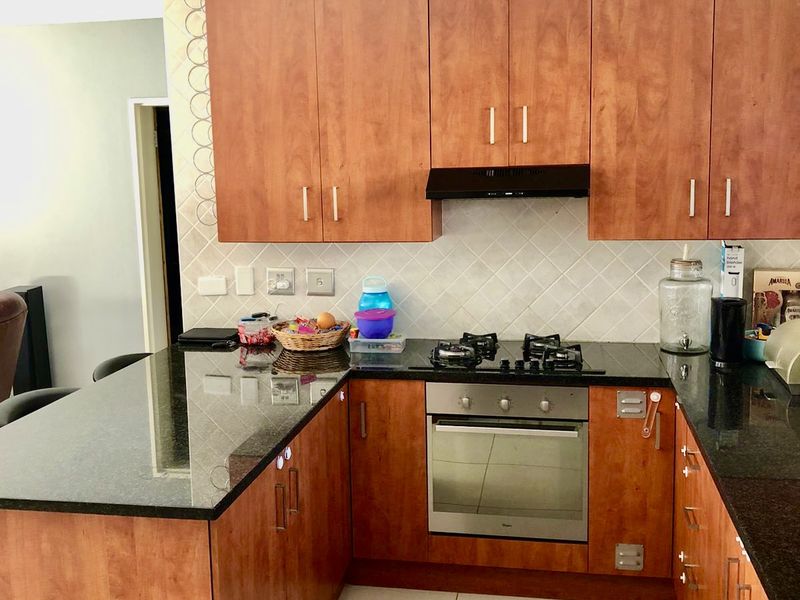 A functional kitchen featuring warm-toned wooden cabinetry, dark granite countertops, a built-in gas hob, oven, and a tiled backsplash.