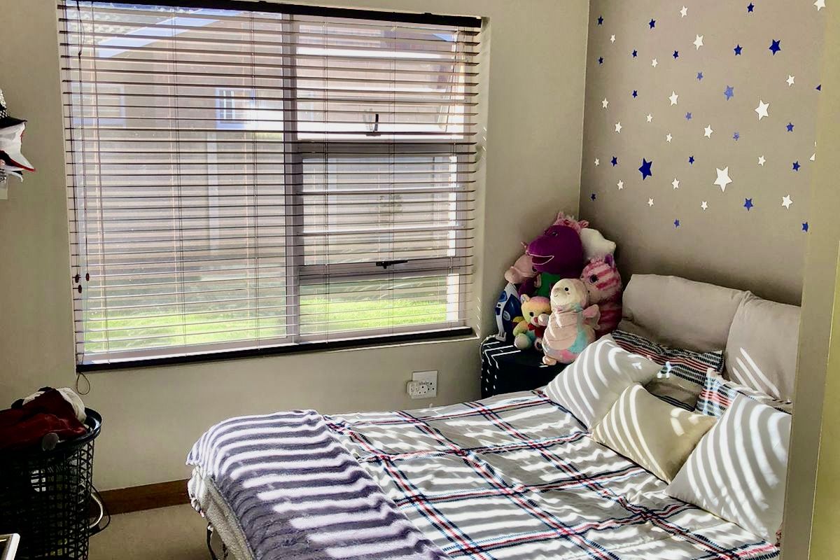 A standard bedroom featuring neutral wall paint, carpeted flooring, and a window fitted with venetian blinds.