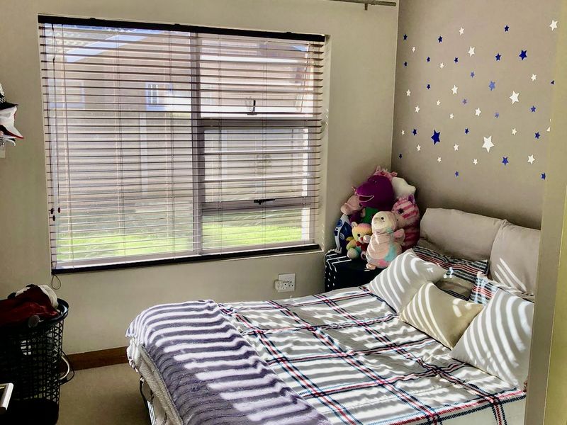 A standard bedroom featuring neutral wall paint, carpeted flooring, and a window fitted with venetian blinds.