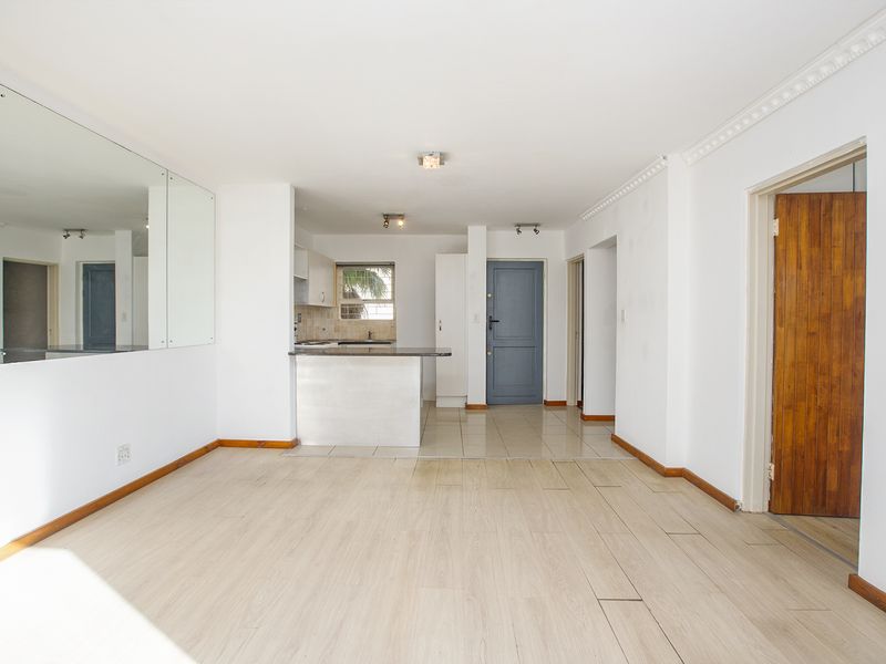 An open-plan living and kitchen area featuring laminate flooring, a breakfast bar, and neutral finishes, offering a blank canvas for interior design.
