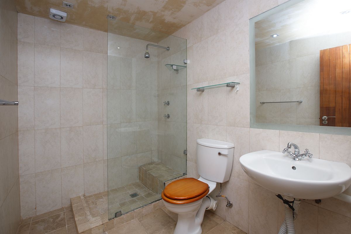 A functional bathroom featuring a walk-in shower with glass screen, pedestal basin, and toilet, finished with neutral wall and floor tiling.