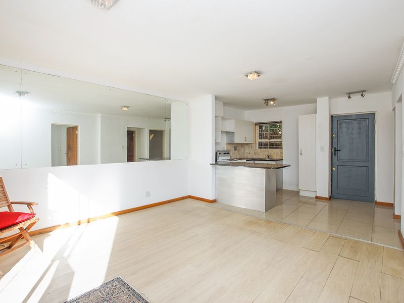 Open-plan living area featuring a compact kitchen with granite countertops, tiled and laminate flooring, and a large wall-mounted mirror.