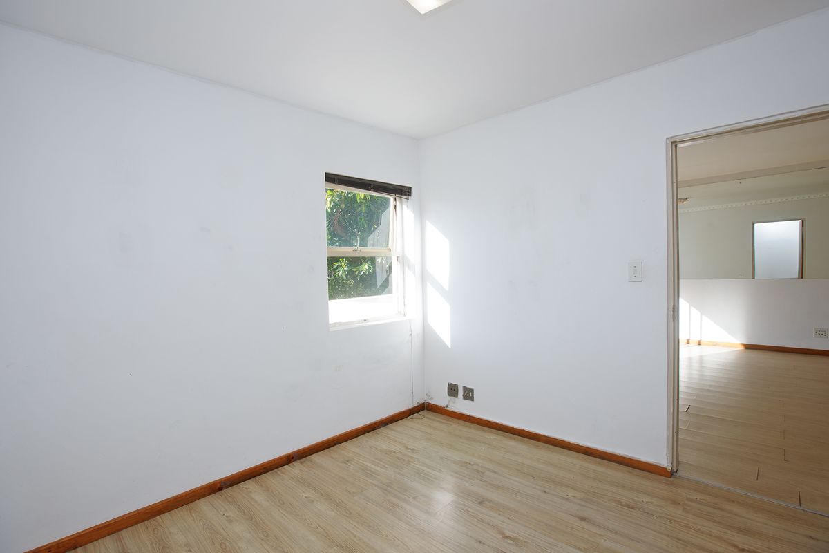 An empty bedroom featuring laminate flooring, white walls, and a window, offering a blank canvas for personalization.