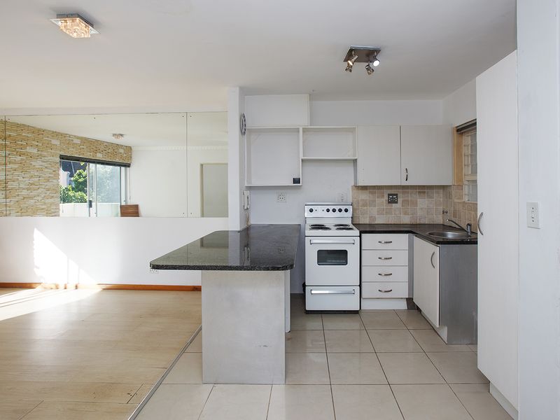 Open plan kitchen and living area featuring granite countertops, tiled flooring, and a mirrored wall, offering a functional space ready for modern updates.