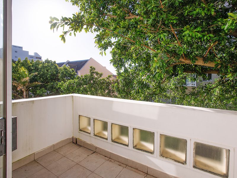 A private balcony featuring tiled flooring and decorative glass block inserts, offering a leafy outlook and direct access via a sliding door.