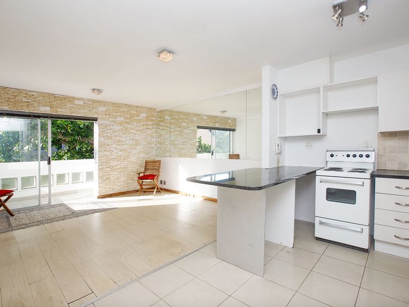 Open-plan living and kitchen area featuring a stone-clad feature wall, mirrored wall, granite breakfast bar, and direct access to a balcony through sliding doors.