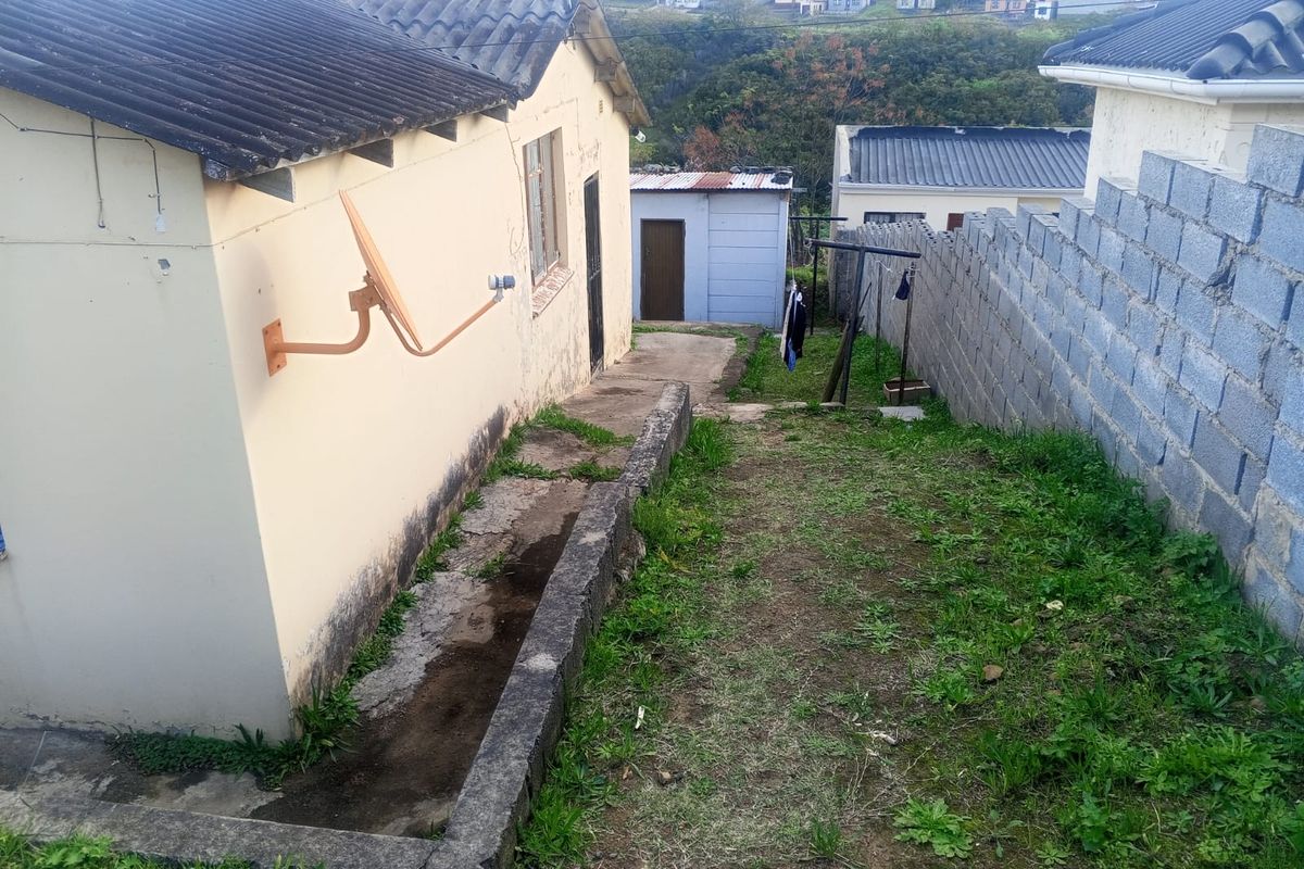 Rear exterior view of the property showing a concrete pathway, boundary wall, and basic building structure with visible signs of wear and maintenance needs.