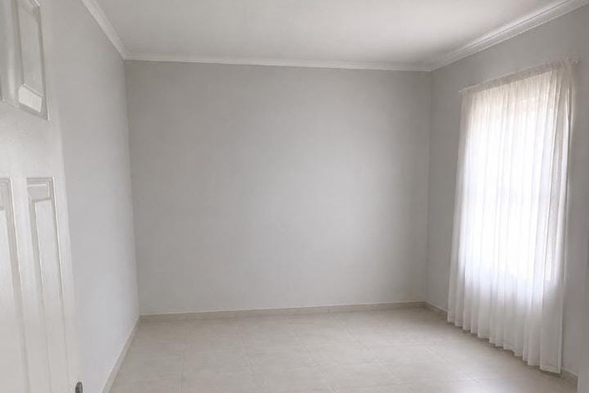 A bright, empty bedroom featuring neutral tiled flooring, coved ceilings, and a classic panel door, offering a clean canvas for personalization.