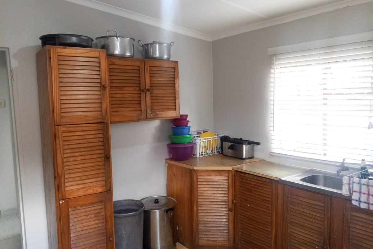 A functional kitchen featuring wooden cabinetry, a stainless steel sink, and venetian blinds, offering a dated aesthetic with potential for modernization.