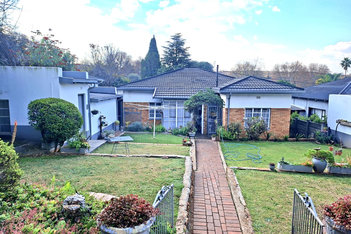 A rear view of the house featuring a brick pathway leading to the entrance, surrounded by a landscaped garden and lawn area.