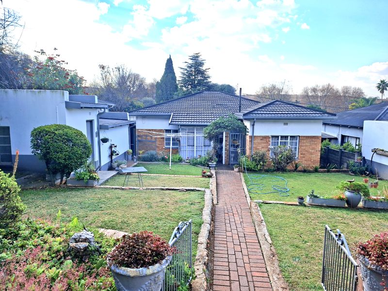 A rear view of the house featuring a brick pathway leading to the entrance, surrounded by a landscaped garden and lawn area.