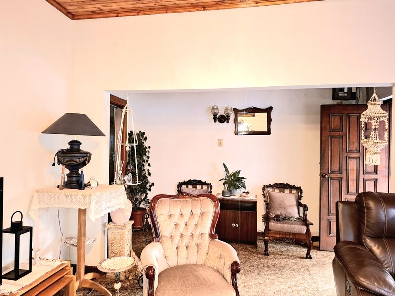 A living room area featuring a timber ceiling, solid wood door, and wall sconce lighting, with carpet flooring throughout.