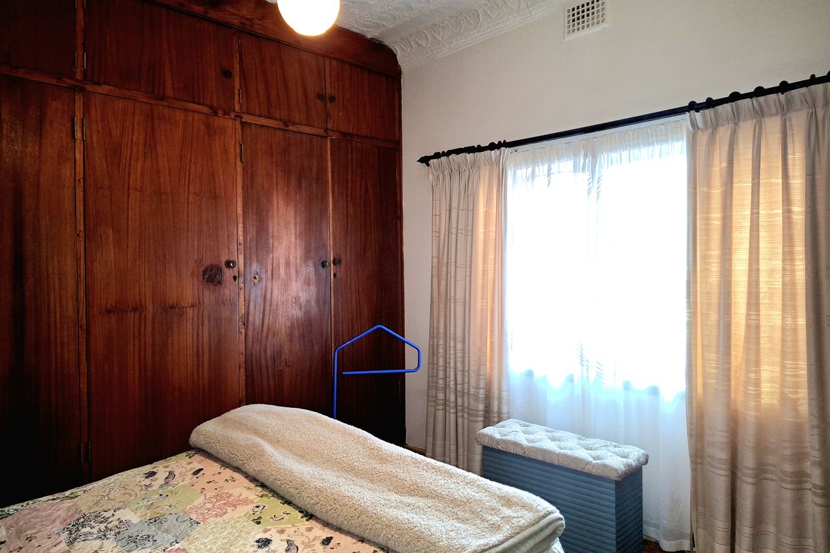 A bedroom featuring a large built-in timber wardrobe, ornate plaster ceiling detailing, and natural light through the window.
