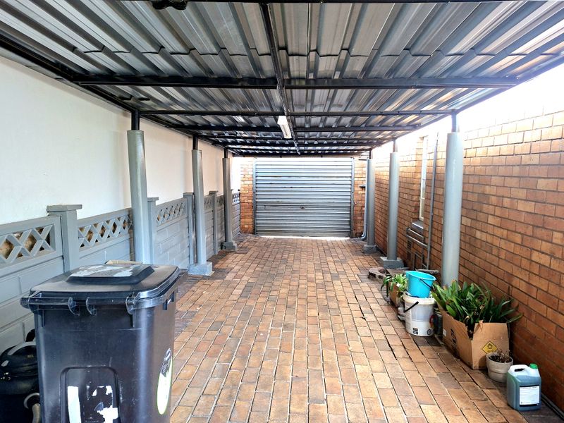 A covered outdoor parking area featuring a corrugated metal roof, brick walls, and paved flooring with a secure roll-up garage door.