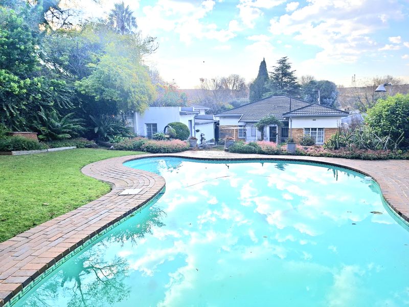 A backyard view featuring a swimming pool with brick coping, surrounded by a landscaped garden and the rear elevation of the house.